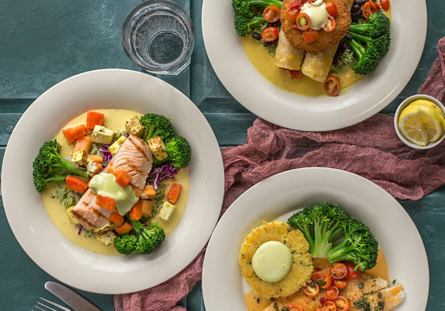 Three plates of food on a table with a glass