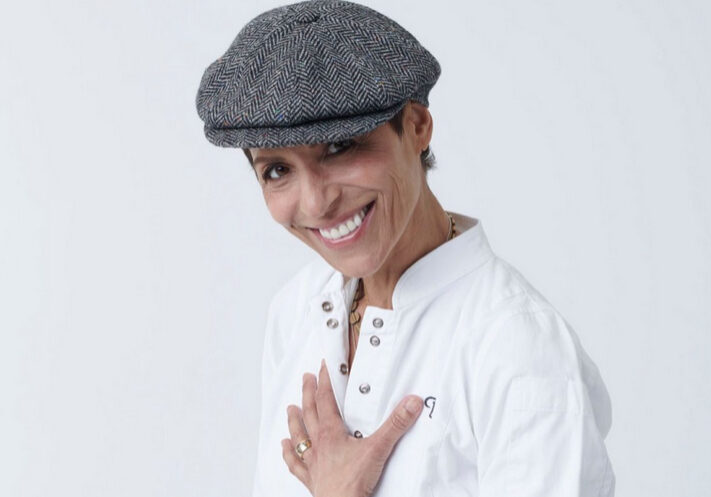 A woman in white shirt and hat smiling.