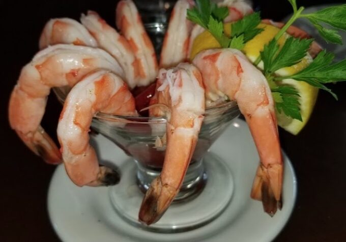 A bowl of shrimp on the table with lemon wedges.