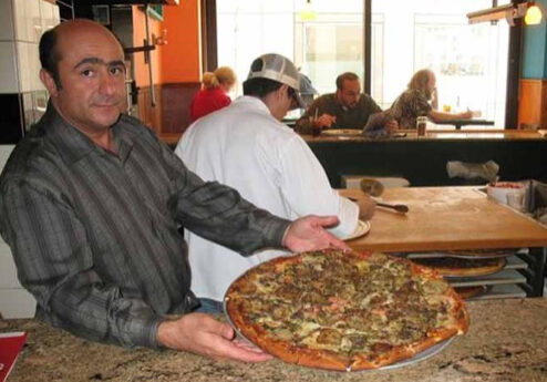 A man holding a large pizza in front of people.