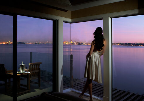 A woman standing in front of the window looking out at water.