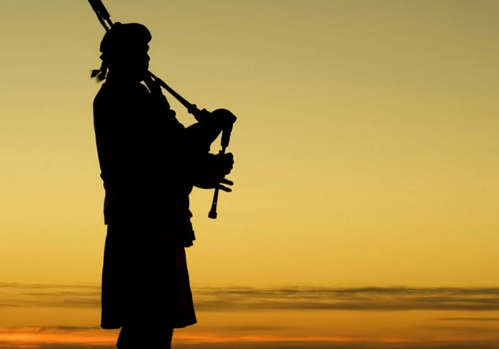 A man playing the bagpipes in front of an orange sky.