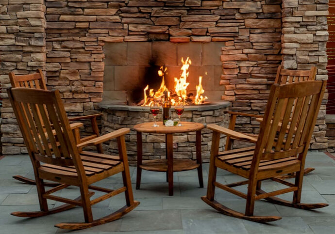 A fireplace with fire burning in it and chairs around.